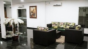A lobby with a reception desk, black sofas, a large mirror, and a painting on the wall. - Apoema Hotel (Cuiabá)