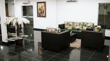 Um hall de entrada com balcão de recepção, sofás pretos, um espelho grande e uma pintura na parede.