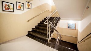 A staircase with a metal handrail, beige walls, and three framed artworks. - Apoema Hotel (Cuiabá)