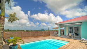 A wooden deck with a swimming pool, a covered seating area, and a view of the landscape.