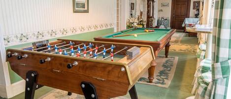 Een kamer met een tafelvoetbaltafel, een pooltafel en een biljarttafel.
