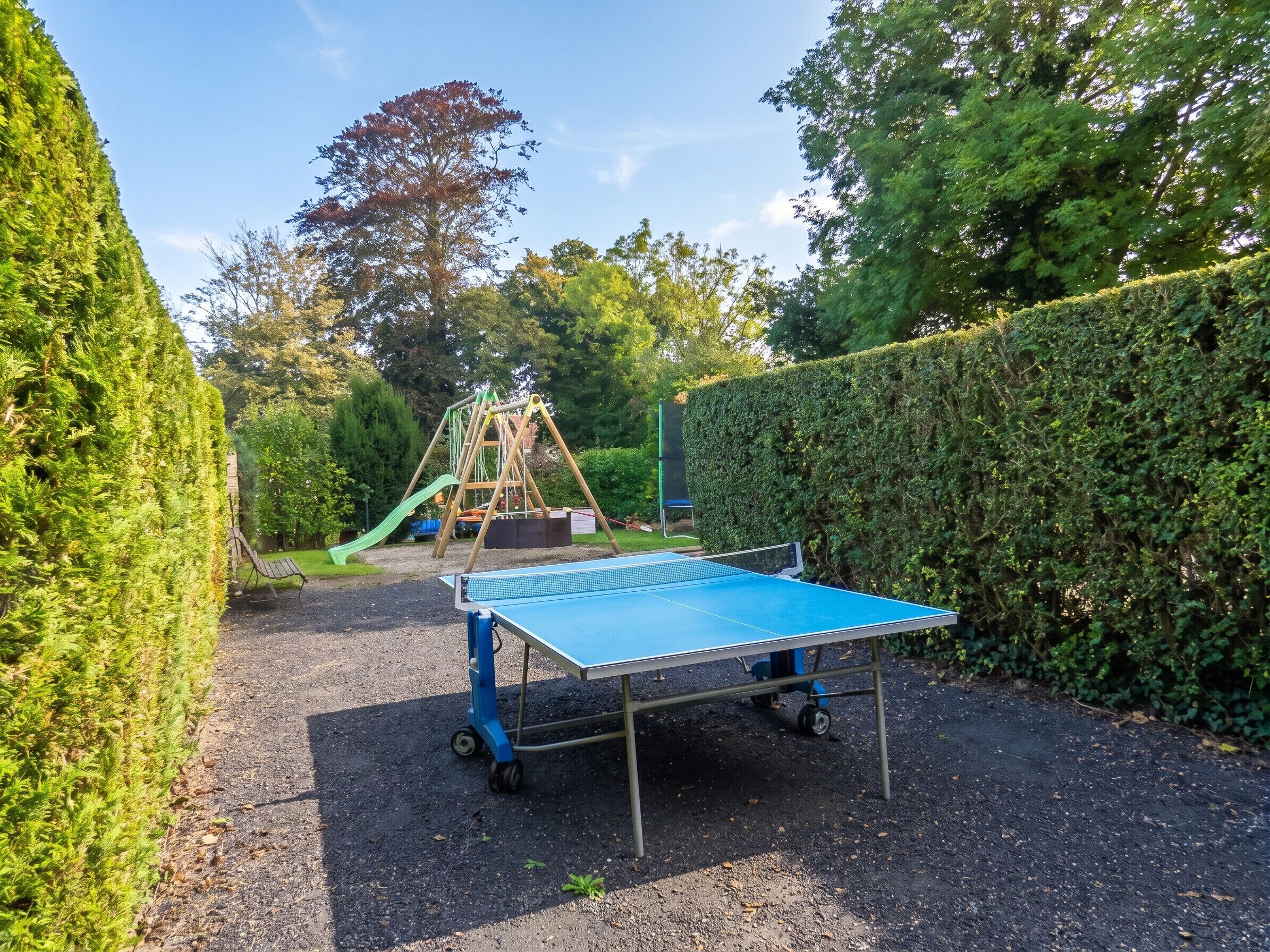 Une table de ping-pong dans un espace extérieur, avec un terrain de jeux en arrière-plan.