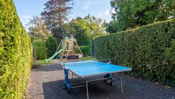 Une table de ping-pong dans un espace extérieur, avec un terrain de jeux en arrière-plan.