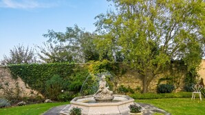 A garden with a fountain, stone wall, and potted plants. - Homerez - Apt. Saint-Martin-des-Entrées (Saint-Martin-des-Entrées)