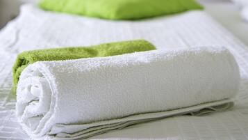 Un lit bien fait, avec un oreiller vert et une serviette blanche enroulée.