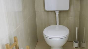 Un bagno piccolo e pulito con un water bianco, un porta carta igienica in legno e una spazzola per il water.