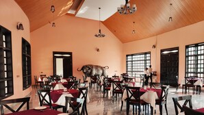 A spacious dining area with high ceilings and large windows, featuring a central bull sculpture. Tables are neatly arranged with white and red tablecloths. - Kiikaloh Grand Resort (Machakos)