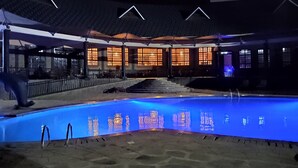 A swimming pool with a blue tint, surrounded by a covered area with traditional-style windows and a staircase leading to an upper level. - Kiikaloh Grand Resort (Machakos)