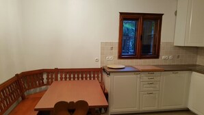 Een knusse keuken met een houten eettafel en bankje, witte kastjes en een raam met uitzicht op groen.