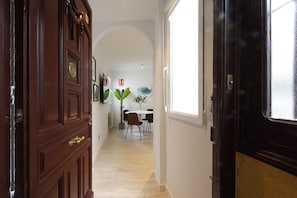 A hallway with a wooden door, a dining area with chairs and a table, and a window with a view. - Sofia II (Madrid)