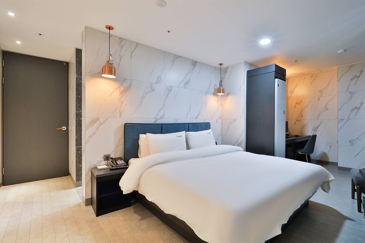 A modern hotel room with a large bed, a desk, and a wardrobe.