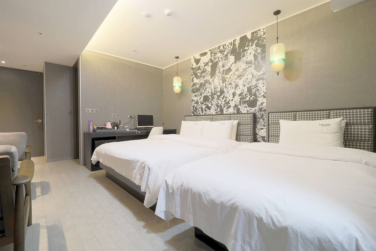 A modern hotel room with two beds, a desk, and a chair.