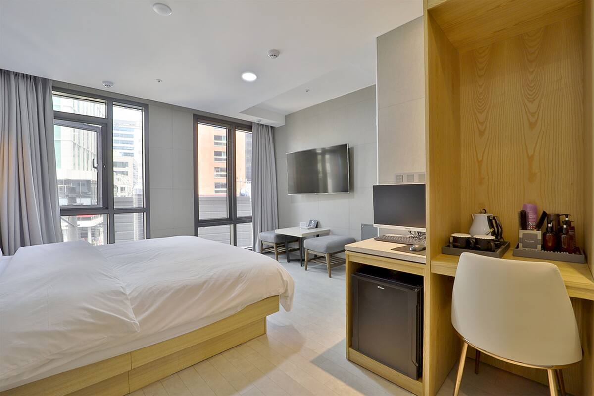 A hotel room with a bed, desk, chair, TV, and a small kitchenette.