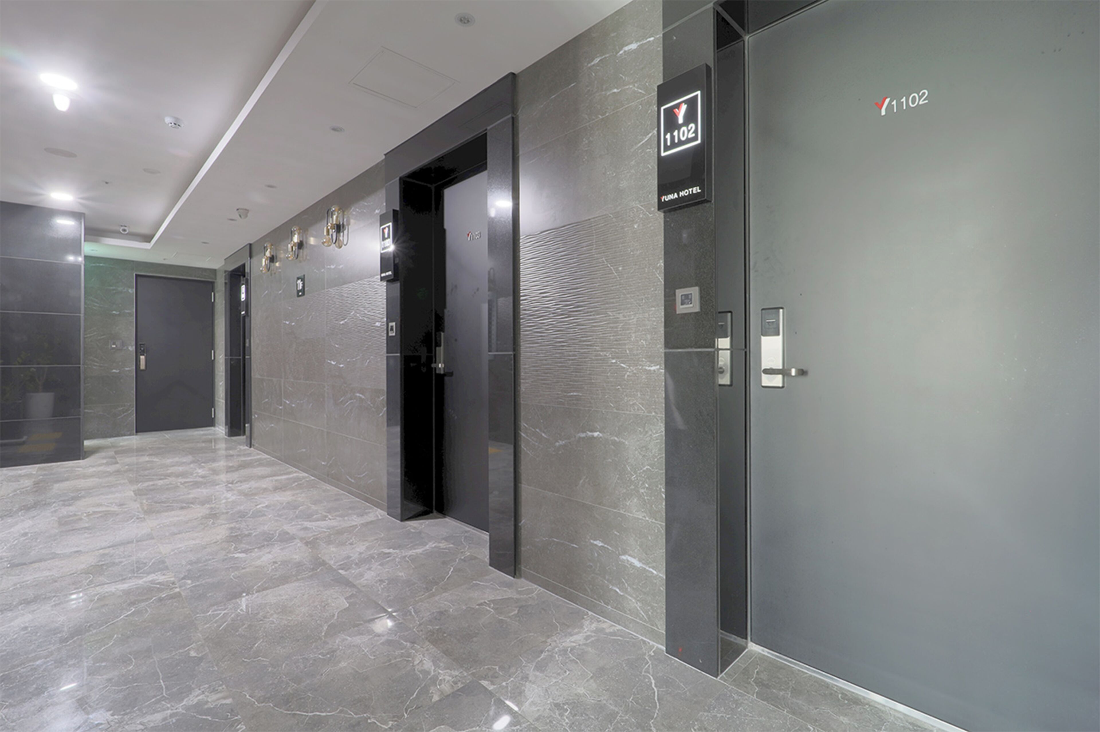 A modern hotel corridor with marble flooring, elevator doors, and a sign indicating room number 1102.