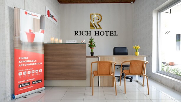 A reception area with a wooden desk, two wicker chairs, a receptionist sign, and a RedDoorz banner. - RedDoorz near Mataram University (Mataram)