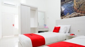 A hotel room with two beds, a white wardrobe, a mirror, and a painting of a rocky landscape. - RedDoorz near Mataram University (Mataram)