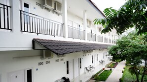 A white building with balconies, outdoor seating, and a garden area. - RedDoorz near Mataram University (Mataram)