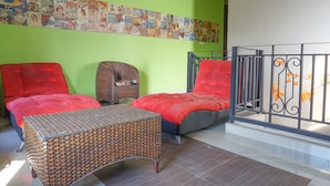 Een kamer met twee rode bekleden stoelen, een rieten tafeltje en een groene wand met een collage over het thema reizen.