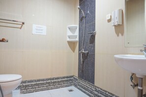 Un baño con inodoro, ducha con cabezal de ducha manual, lavamanos y un cartel en la pared.