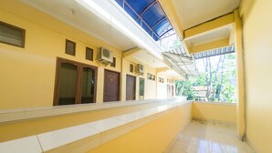 A corridor with yellow walls, white tiled flooring, and a blue ceiling. There are doors and air conditioning units along the walls.