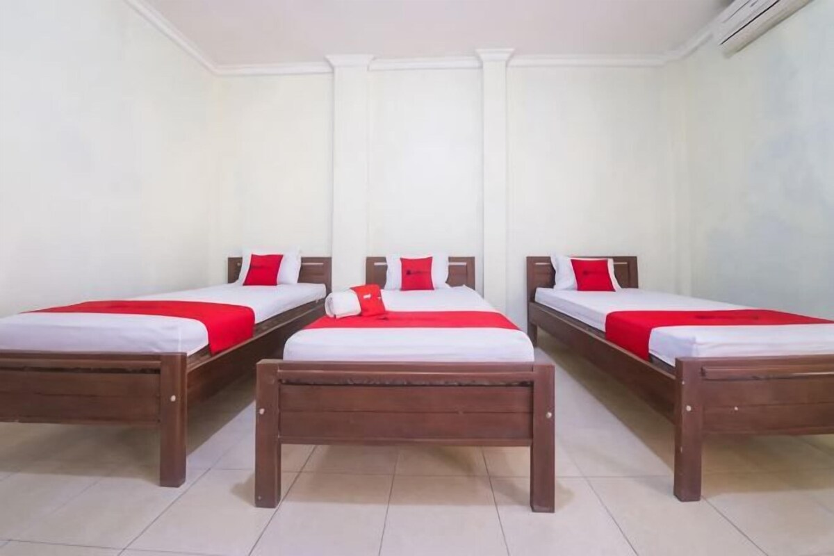Habitación de hotel con tres camas de madera, cada una con ropa blanca y detalles rojos.