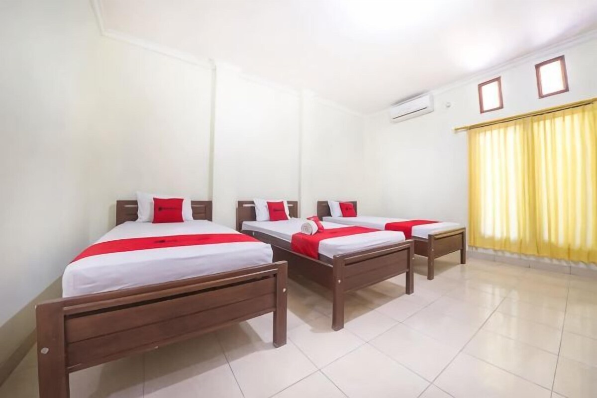 A hotel room with three beds, a small table, and a window with curtains.