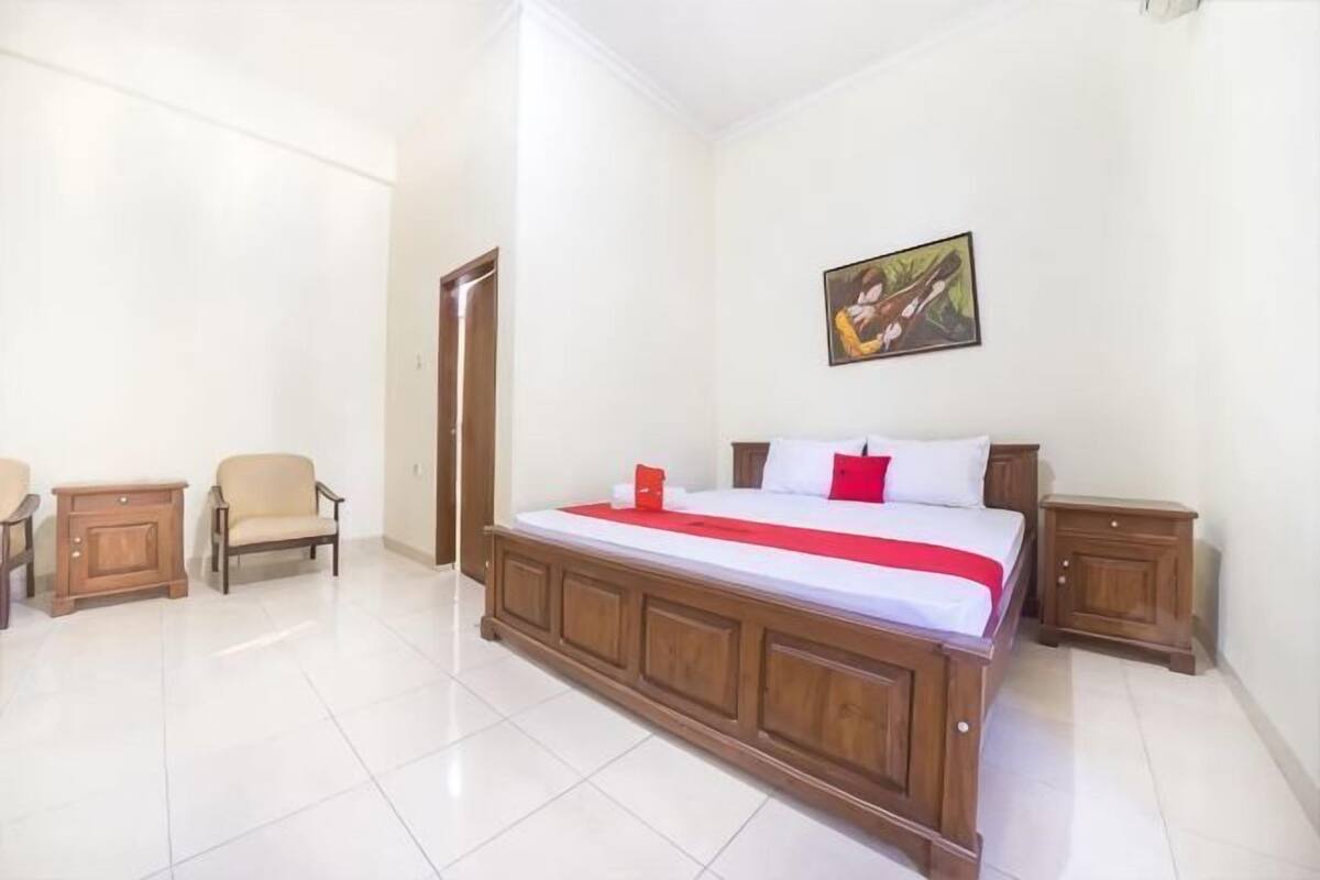 A bedroom with a large bed, a chair, a nightstand, and a painting on the wall.