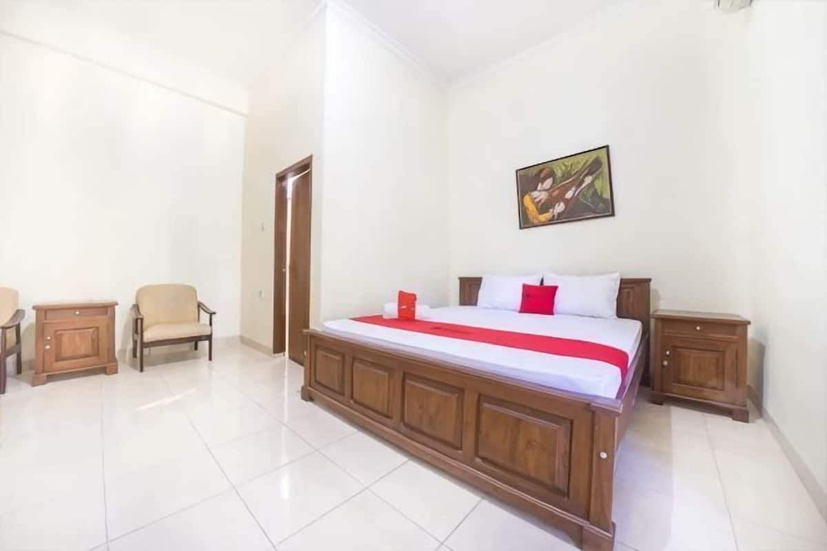 A bedroom with a large bed, a chair, a nightstand, and a painting on the wall.