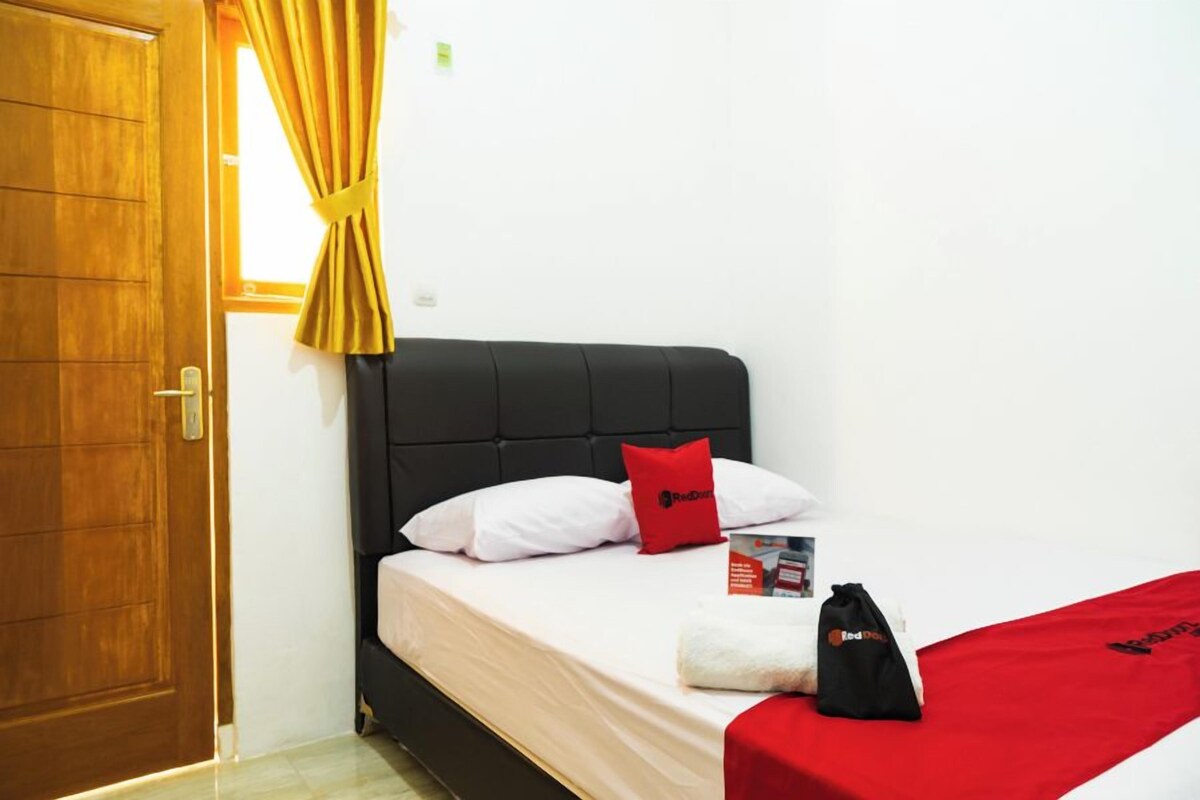 A hotel room with a bed, a door, a window with curtains, and a Red Dot branded bag on the bed.
