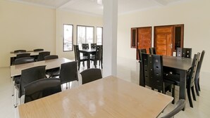 Een vergaderzaal met meerdere tafels en stoelen, grote ramen en een hoge plafond met dakramen.