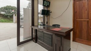 Een receptiebalie met een glazen scheiding, twee monitoren, een houten deur en een betegelde vloer.