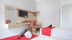 Una habitación de hotel con cama, escritorio, silla, televisor y una toalla roja sobre la cama.