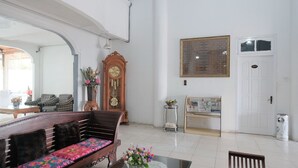 Amplia sala de estar con un sofá de madera, una mesa de comedor con un jarrón de flores, un reloj grande y una puerta con la inscripción '101'.