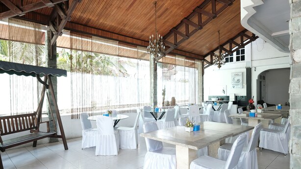Un espacio exterior techado para comer con sillas y mesas blancas, un banco de madera y un candelabro.