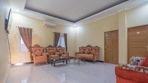 A spacious living room with a sofa set, a coffee table, and a red couch. - RedDoorz Plus near Syamsudin Noor Airport 3 (Banjarbaru)
