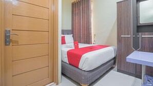 A hotel room with a bed, a wardrobe, a small table, and a curtain. - RedDoorz Plus near Syamsudin Noor Airport 3 (Banjarbaru)