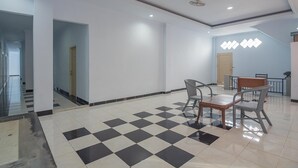 Un vestíbulo amplio con piso a cuadros, una escalera y un área de descanso con sillas y una mesa.