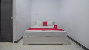Una cama pequeña y ordenada con un colchón blanco, almohadas rojas y blancas, y una taza roja a un lado.
