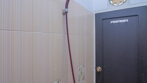 Una ducha con un cabezal rojo, una puerta con cerradura y un ventanal decorativo con un diseño de sol.