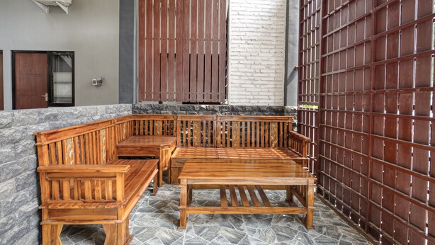 Un banco y una mesa de madera frente a un muro de piedra, con una reja metálica y una puerta al fondo.