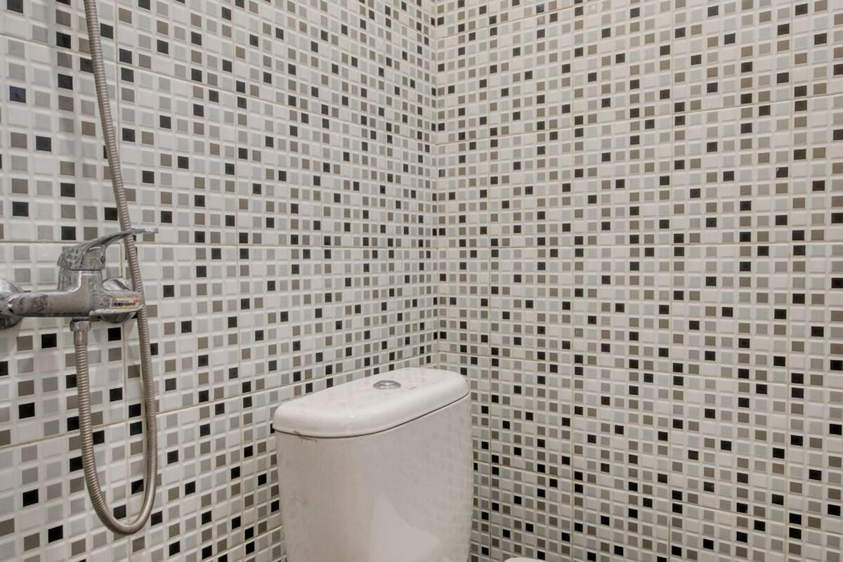 A bathroom with a tiled mosaic wall, a showerhead, and a toilet.