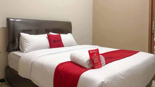 A hotel room with a bed, white bedding, a red throw blanket, and a RedDoorz towel. - RedDoorz Syariah @ Jl. Cengger Ayam Dalam (Malang)