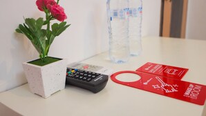 A small potted plant with pink flowers, a remote control, two water bottles, and a red card on a white surface.