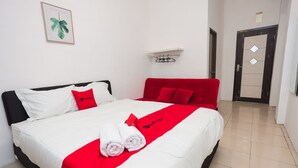 A neatly made bed with white and red bedding, a red pillow, and two rolled towels.