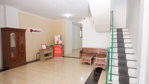 A hotel lobby with a reception desk, a staircase, and a RedDoorz sign.