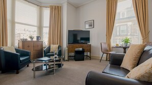 A living room with a sofa, armchair, coffee table, TV, and a desk with a computer. - Rowntree Lodge (Scarborough)