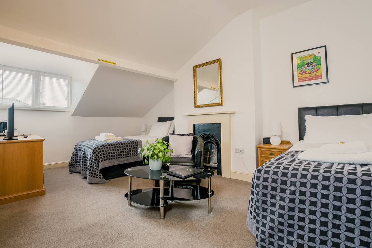 A bedroom with two beds, a desk, a chair, a fireplace, and a window.