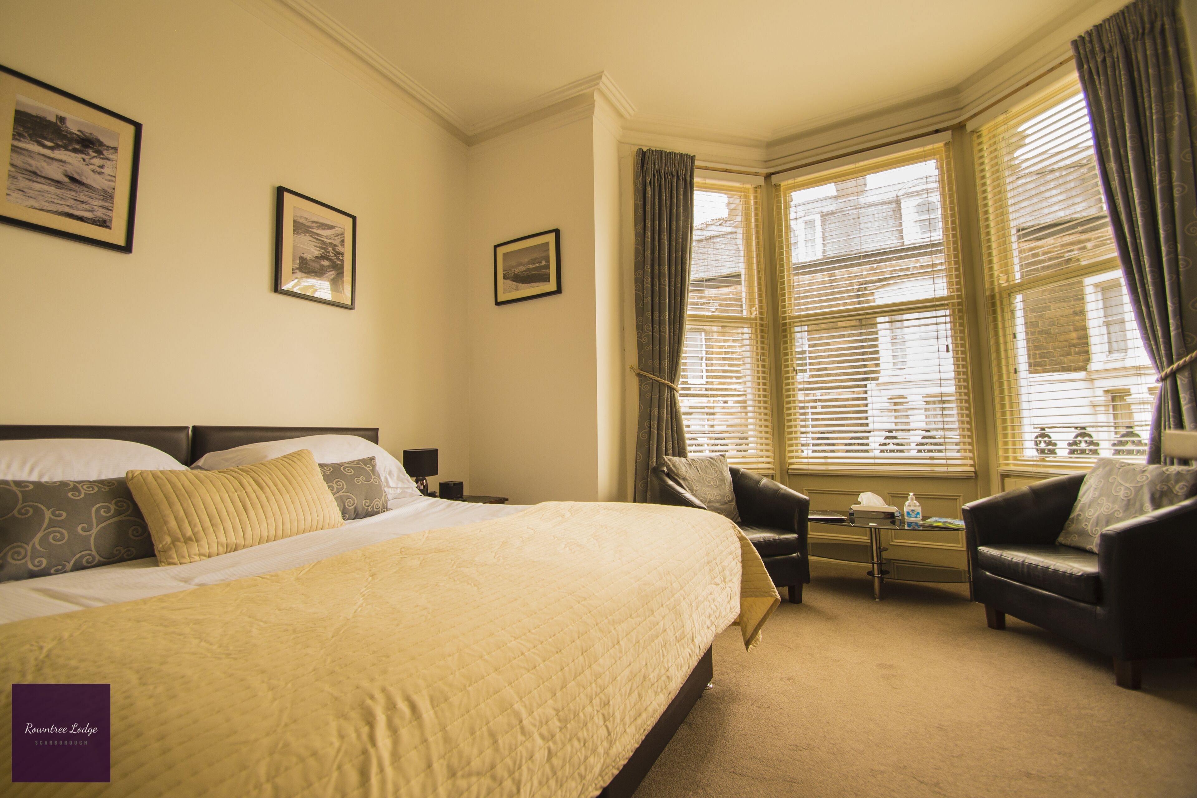 Una habitación de hotel con una cama grande, un sofá, una mesita y una ventana con cortinas.