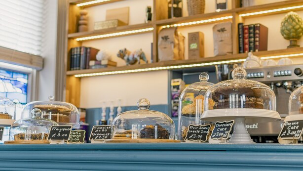 A bakery display with various baked goods under glass domes, each with a price tag. - Rowntree Lodge (Scarborough)