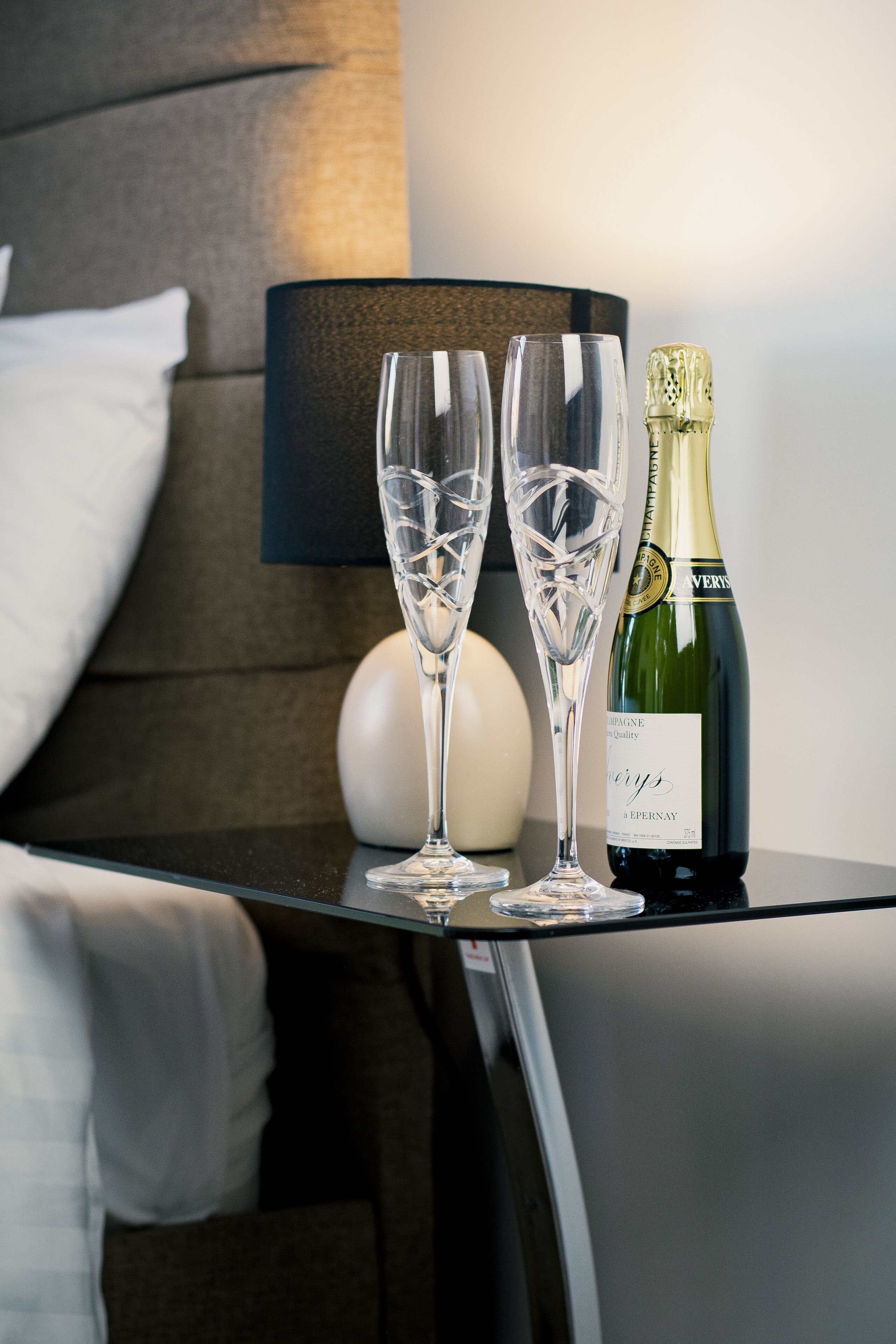 A neatly arranged table with two champagne flutes and a bottle of champagne in a hotel room.